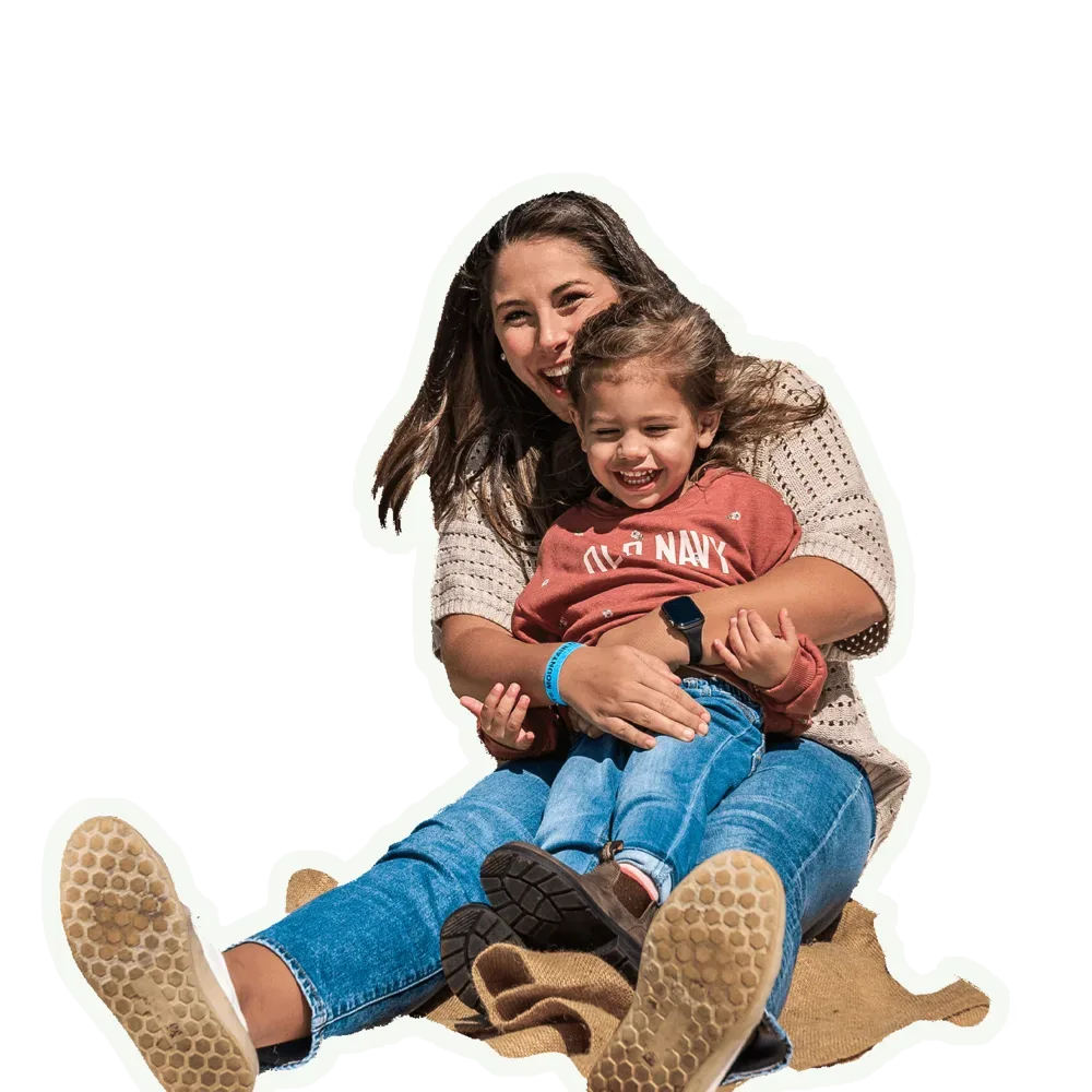 A mom and daughter laughing together at the bottom of the slide